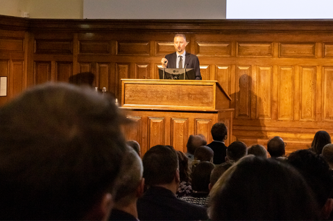 Man stood behind a lectern in front of an audience
