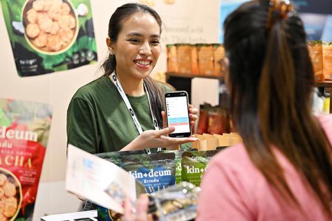A smiling woman showing information about a product on an iphone to another woman over a stand at the International Food & Drink Event