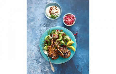 A plate of lamb cutlets with garnish and side dishes on a blue table