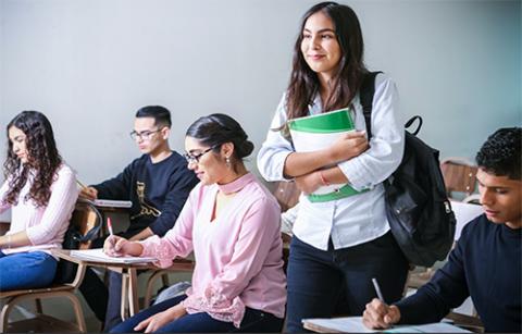 Girl standing and smiling in a classroom holding books