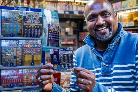 Man in a convenience store smiling holding up a lottery card