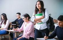 Girl standing and smiling in a classroom holding books